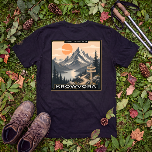 A black graphic 100% cotton hiking t-shirt laid flat on a bed of green grass, leaves, pinecones, hiking boots, and trekking poles. The t-shirt features a retro-style mountain landscape graphic with the text 'SUMMIT COLLECTION' and 'KROWVORA'.
